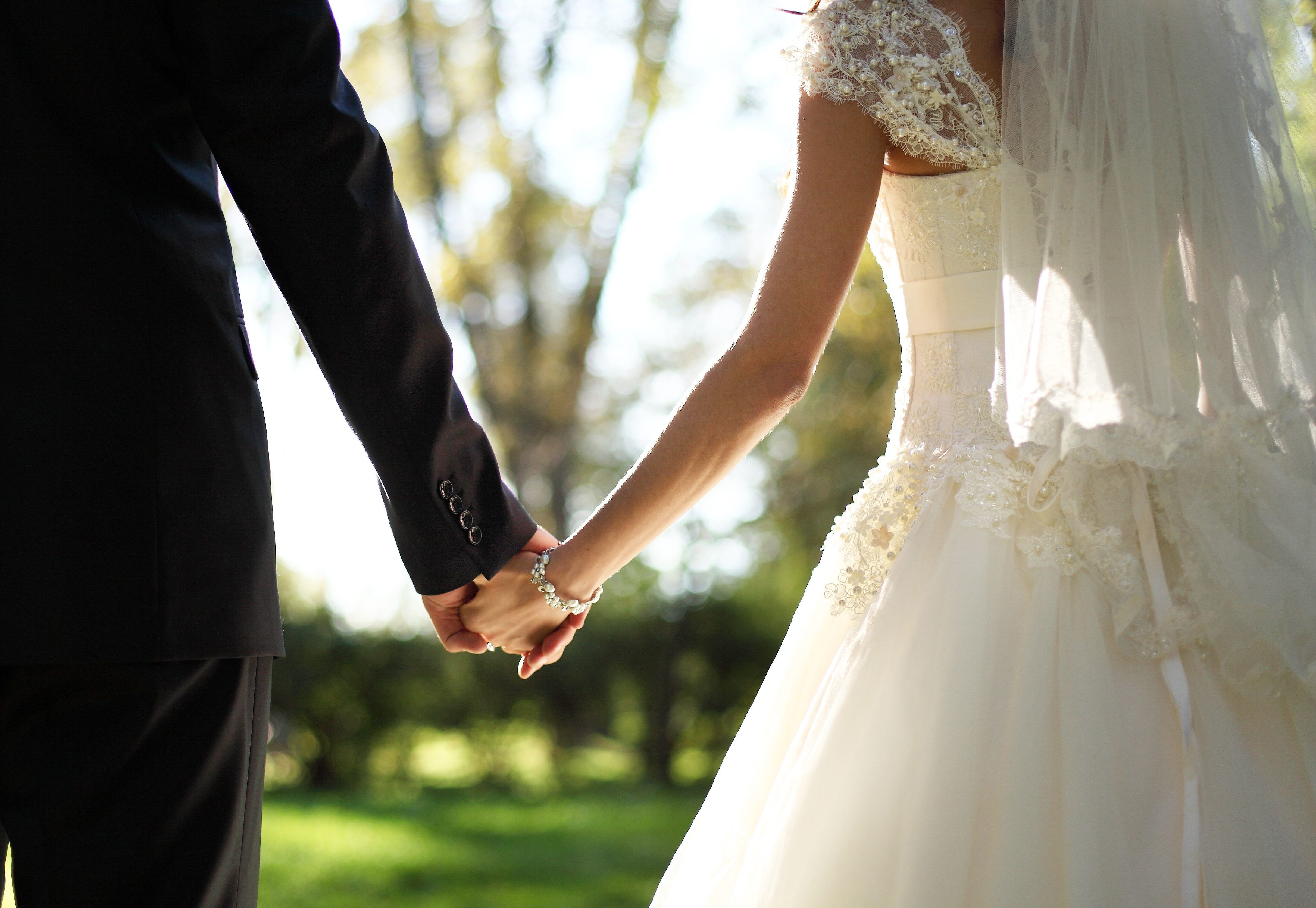 a bride and groom hold hands as they walk through the grass