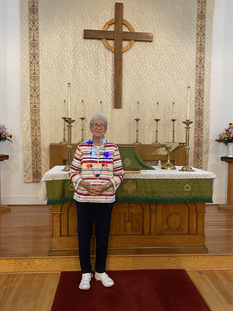 an older woman standing in front of a cross